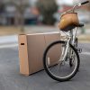 Women's bicycle with wicker basket, posed beside C1033 bicycle box, showing side handles