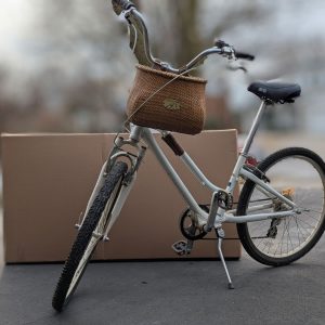 Women's bicycle with wicker basket, posed in front of C1033 bicycle box