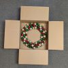 Wreath box with flaps open, containing a red, green and silver wreath