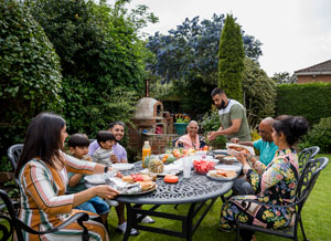 Smiling family gathers around a lovely table in a lush green backyard to share a meal