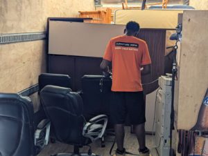 A Furniture Bank mover (wearing an orange T-shirt with the Furniture Bank logo and the slogan 