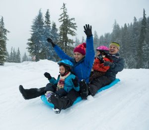 Mother, father, two children tobogganing down a snowy hill